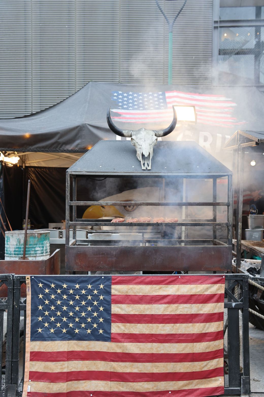 A smoking barbecue grill under American flags