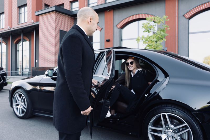 A chauffeur holding the rear door of a black Mercedes-Benz for a passenger