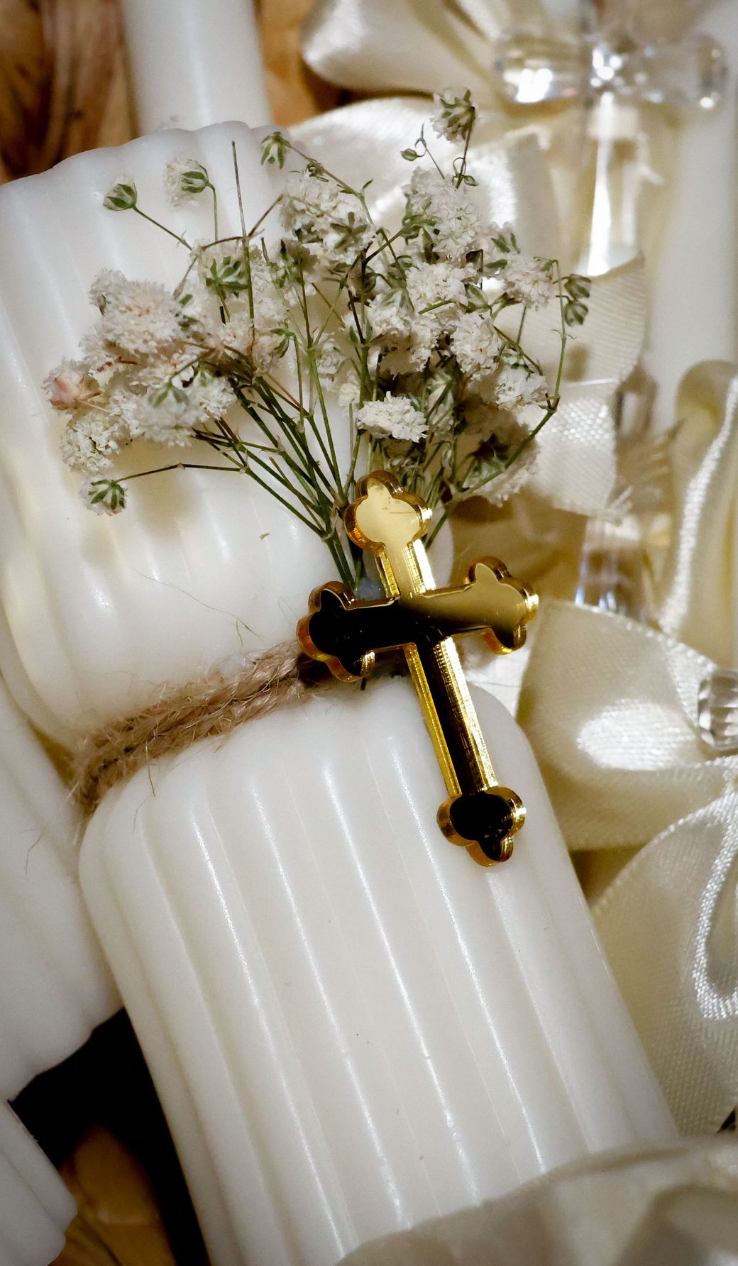 A white candle with a gold cross and baby’s breath