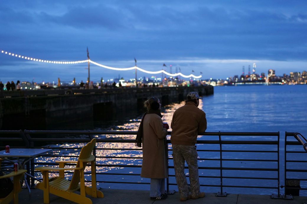 A couple watching city lights across the water at dusk