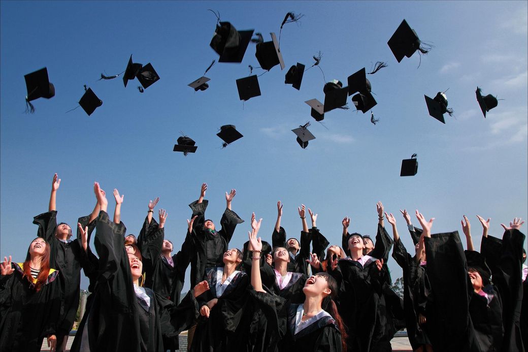 Graduates in black gowns throwing their caps into the sky