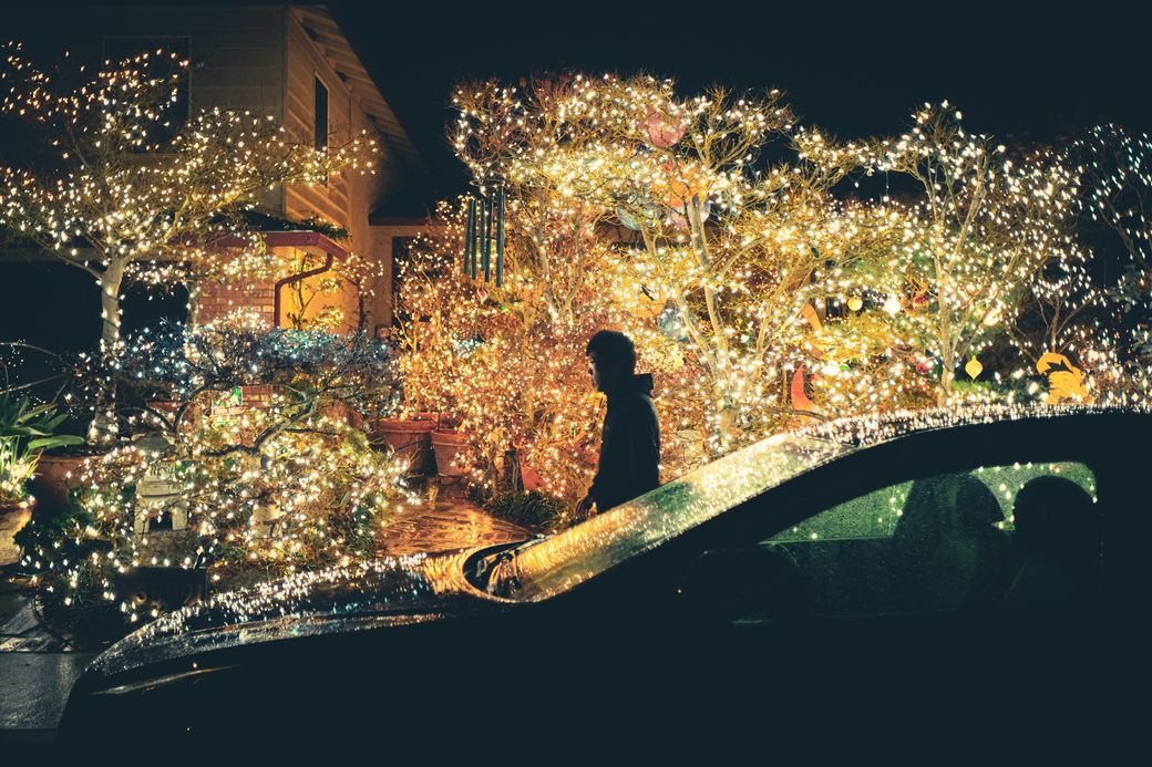 A house covered in Christmas lights at night, seen past a car roof