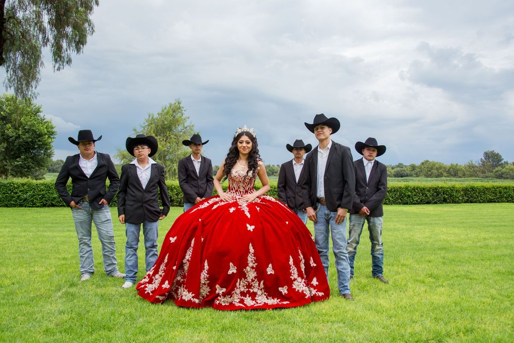 A quinceañera in a red ball gown with her court of chambelanes in cowboy hats
