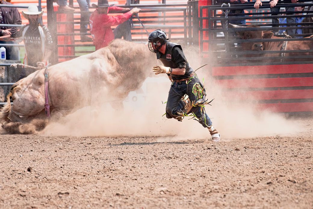 A bull rider running clear of a bucking bull in a dusty rodeo arena