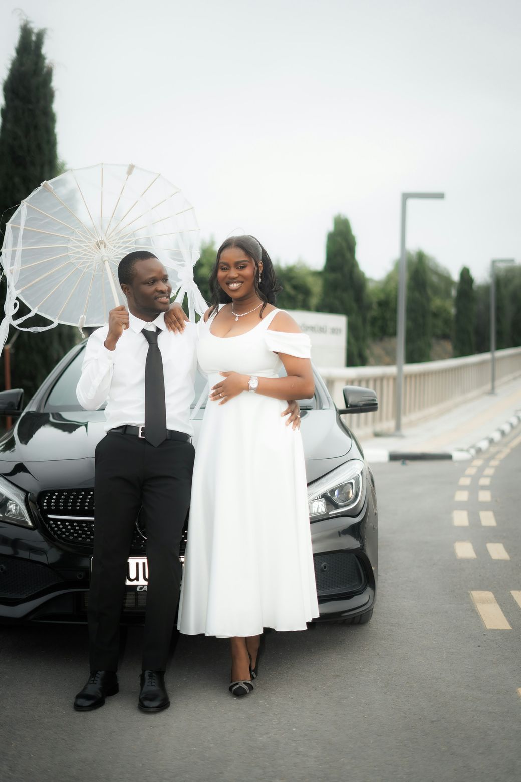 A newly married couple in front of a black Mercedes-Benz sedan